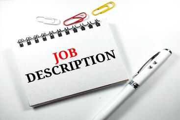 A card that states job description and has paper clips and pens around it